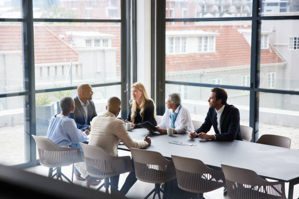 Businesspeople talking together during a meeting in an office boardroom Diverse group of businesspeople talking together around a conference table during a boardroom meeting in a modern office board room stock pictures, royalty-free photos & images