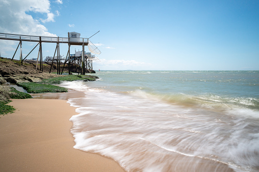 North Atlantic ocean waves washing over sandy beach near seaside tourist resort Royan, Charente-Maritime, France and traditional fishing huts on rocky shores