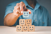 A man's hand placing a wooden cube block form with a smiling symbol. The notion of a satisfaction survey is based on the top superb company services rating client experience.