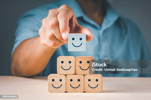 A Mans Hand Placing A Wooden Cube Block Form With A Smiling Symbol The Notion Of A Satisfaction Survey Is Based On The Top Superb Company Services Rating Client Experience Stock Photo - Download Image Now
