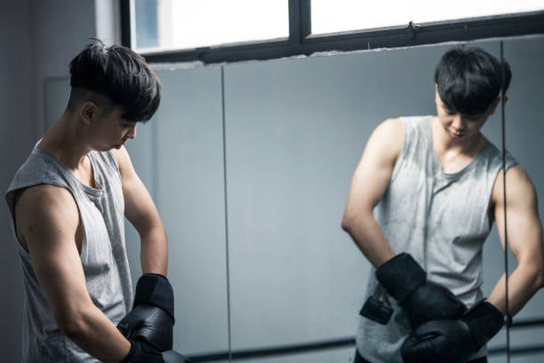 Muscular Asian Man putting on boxing gloves in front of mirror stock photo