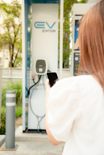 A woman is using a phone to operate an electric car charger.