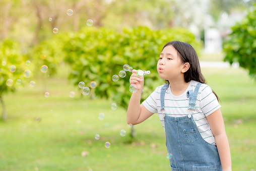 A cute girl is having fun blowing bubbles in the middle of a meadow and green trees.