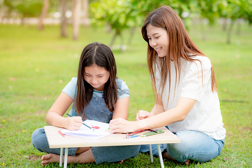 Mother or teacher teaching a girl to draw and paint outside.