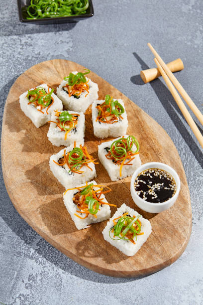 マキは、現代的な構成で木製のボード上に揚げニンジンとネギの上にロール。コンクリートのテーブルに箸を置いて寿司を巻きます。最小限のスタイルで巻寿司。 - appetizer asia carrot maki sushi ストックフォトと画像