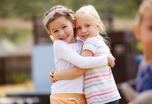 Double portrait in studio, in front of bright grey background: younger brother and teenage sister, looking into camera and smiling, boy with hands on girls shoulder