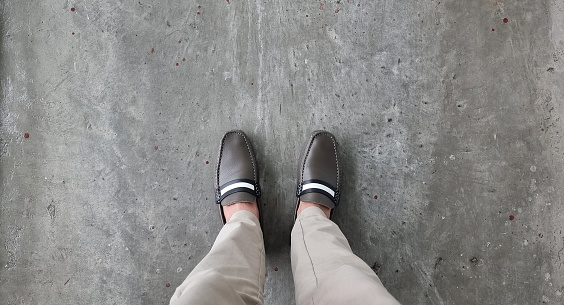 businessman in brown vintage casual shoes and beige slacks seen form above. relax standing of young businessman on grey concrete floor. fashion and footwear concept, close up of man legs.