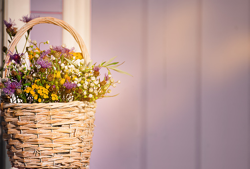 Bouquet of wild flowers in a wicker basket against the background of a lilac wooden wall