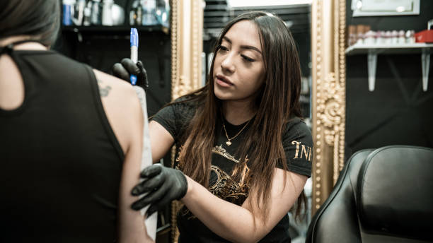 istock Mexican female Tattoo artist creating art on client arm 1395563396