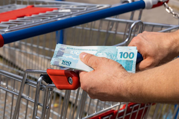 cesta de compras de um supermercado e dinheiro brasileiro mantido em mãos, conceito de inflação, compras mais caras e o orçamento familiar - real food fotos - fotografias e filmes do acervo