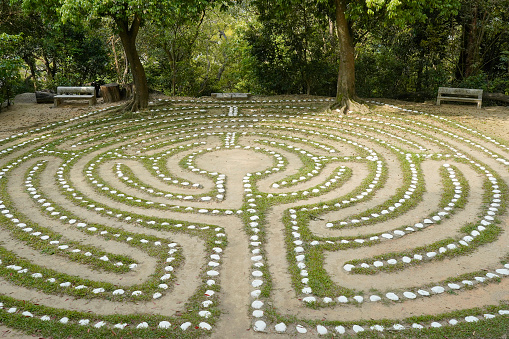 Circular stone labyrinth in garden with green trees and benches.