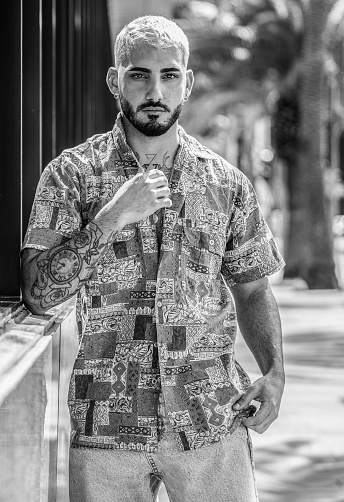 Portrait of handsome young man in casual clothing looking at camera, posing outdoor. Fashionable guy with tattoos, beard and mustache. Real people.