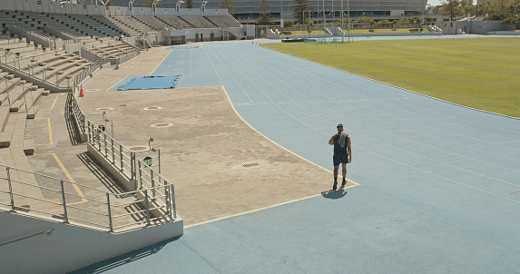 An unrecognizable man walking on a track at a stadium. Rear view of a male athlete training outdoors. Sport, wellness and fitness