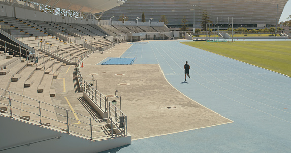 An unrecognizable man running on a track at a stadium. Rear view of a male athlete training outdoors. Sport, wellness and fitness