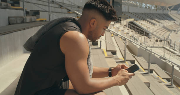 istock A male athlete using a smartphone at a stadium. Young man taking a break after playing sport and browsing online with his phone 1395566424