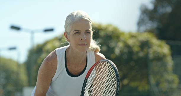 dojrzała kobieta trzymająca rakietę i grająca w tenisa na odkrytym korcie - action tennis women tennis racket zdjęcia i obrazy z banku zdjęć