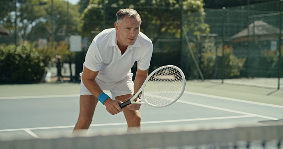 Mature man holding a racket and playing a game of tennis at an outdoor court