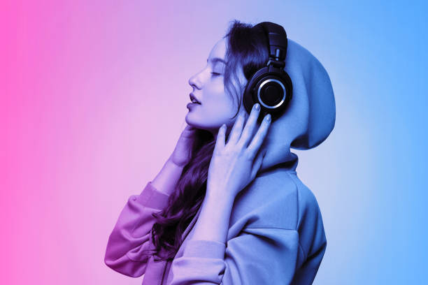 ragazza in una felpa con cappuccio oversize che indossa cuffie wireless, faccia di profilo. rosa neon e tonificazione blu. - wireless technology holding caucasian one person foto e immagini stock