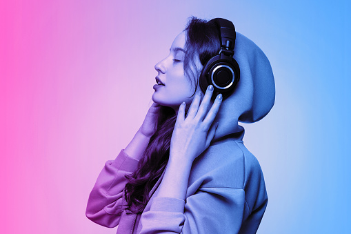 Girl in an oversized hoodie wearing wireless headphones, face in profile. Neon pink and blue toning.