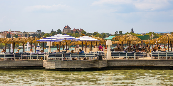 Lake Annecy view with tourists lunching under the beach umbrellas of a restaurant on the banks of the lake on a summer day in France