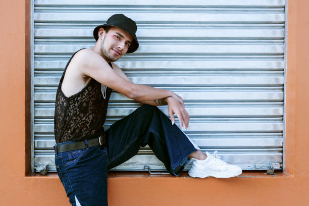 istock Handsome young man with eye makeup casually posing on a coral-colored wall with a metal shutter 1395569359