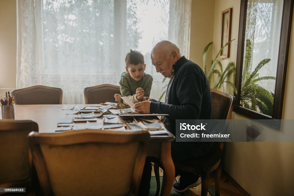 Grandfather showing pictures to grandson Grandfather and grandson sitting at the table and looking at old pictures together at elderly man's home. Family Tree Stock Photo