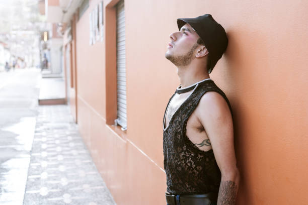 Man from the lgbti+ community leaning against a coral-colored wall and looking up at the sky. Strolling through a Latin American town. stock photo