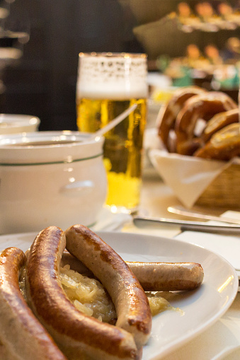 Close up Appetizing German Recipe with Sausage. Classic German dinner of fried sausages with braised cabbage on large white plates with light beer, standing on table in restaurant interior.