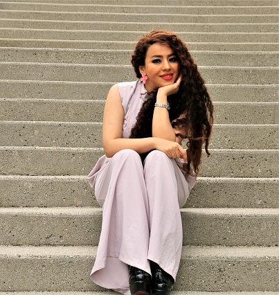 A Middle Eastern woman sitting on a concrete staircase. She is wearing a pink sleeveless pant suit.