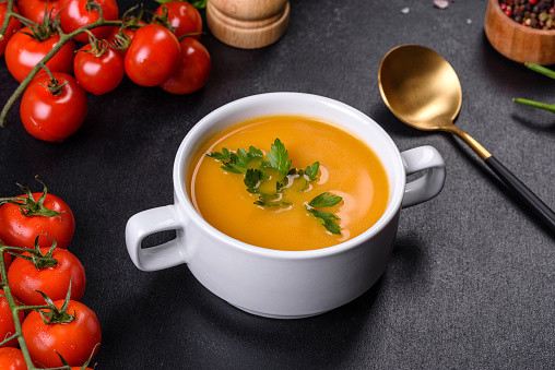 Delicious fresh pumpkin puree soup decorated with parsley in a white plate against a dark concrete background