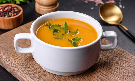 Delicious fresh pumpkin puree soup decorated with parsley in a white plate against a dark concrete background