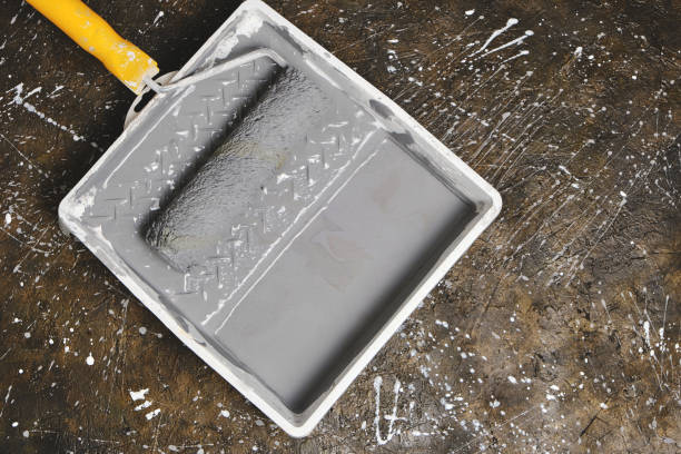 istock Paint roller with yellow handle in tray for roller with gray paint on concrete floor. 1395580978