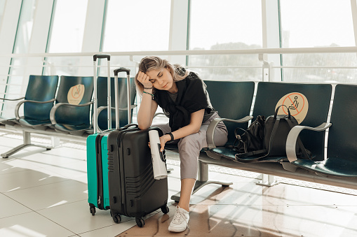 Mujer rubia aburrida con equipaje, apoyando el codo en las maletas, sentada en la sala de espera en el aeropuerto debido a la restricción de viaje de Covid photo