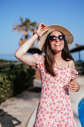 young woman with summer clothes putting on her hat and laughing, vertical portrait