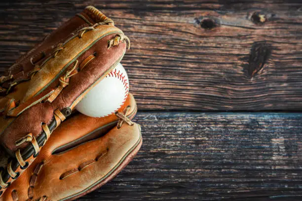 Leather baseball or softball glove with ball on rustic wooden background with copy space.