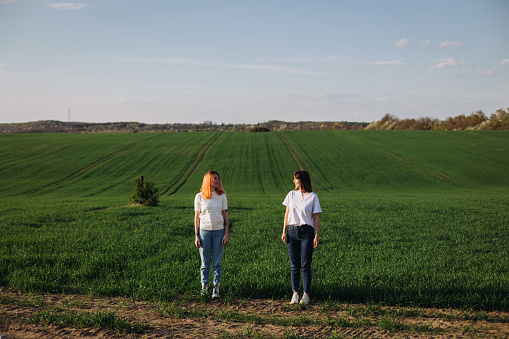 Two women in a white shirt standing among the green agricultural field in a springtime