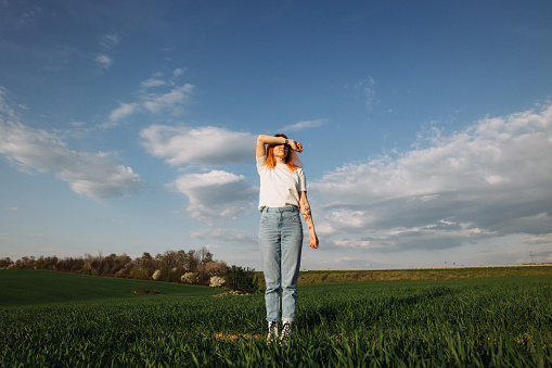 A beautiful woman in white shirt standing among green agricultural field in a springtime