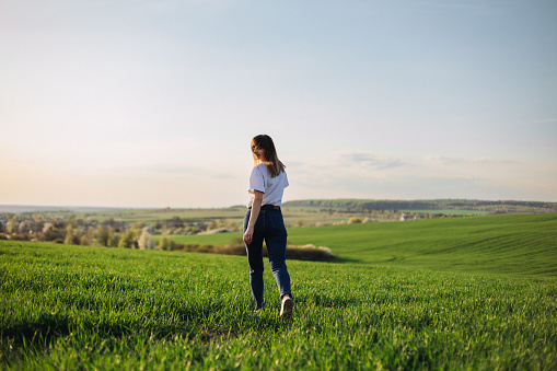 A beautiful female farmer walking on the green agricultural field in a spring