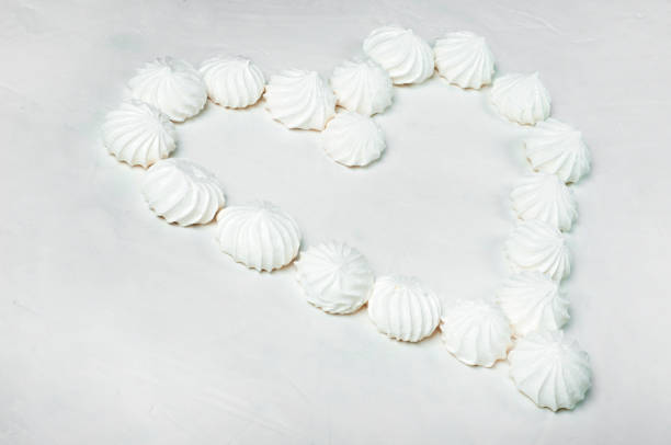 from meringue cakes - a French dessert, a heart shape with an empty middle on a gray background is laid out. Meringue is made from a mixture of beaten egg whites with sugar.