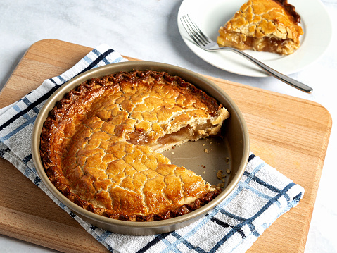 Fresh out of the oven, an apple pie cools off with a slice on a plate with a fork.