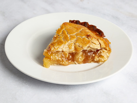 Slice of apple pie on a white plate and marble surface.