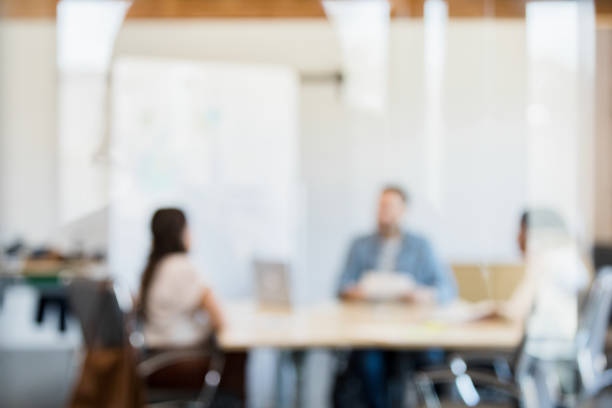 A defocused photo of a multiracial group of three employees as they meet together in the conference room.