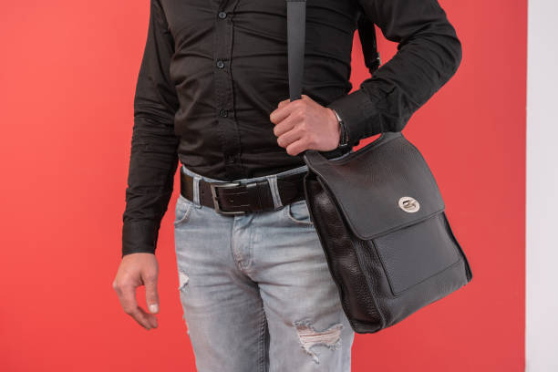 istock Man standing in blue jeans and holding black hand bag over colored background. 1395593201