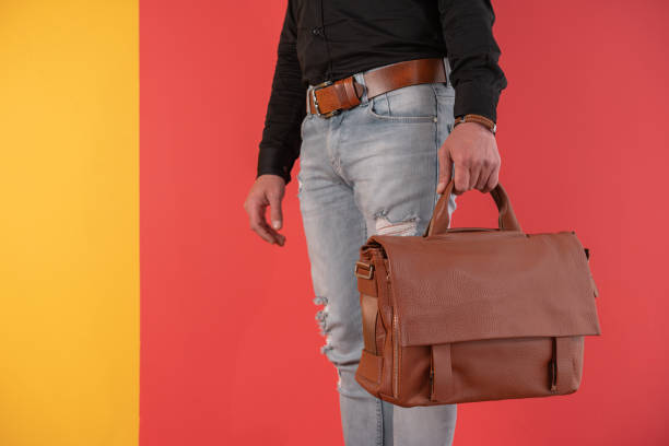 istock Man standing in blue jeans and holding brown hand bag over colored background. 1395593376
