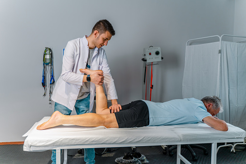 Physiotherapist stretching senior man's legs