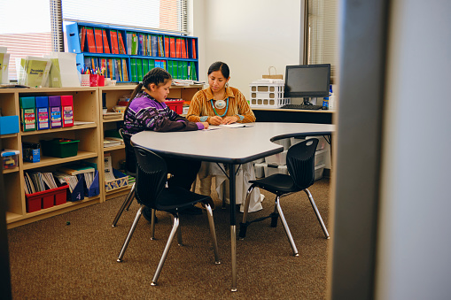 A Native American Navajo elementary age student in a school classroom working with a teacher individually.