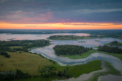 Amazing lake land from above, beautiful islands covered with trees and meadows in morning sunlight. Aerial, flight over lakes during fantastic sunrise. Colorful clouds in sky on horizon.