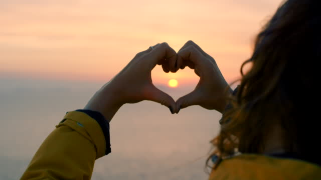 Shot of a unrecognizable female holding a heart shape with her fingers while doing a hike