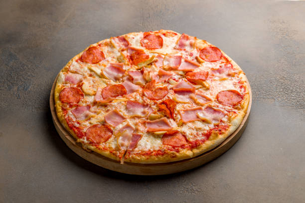 istock Italian meat pizza with chicken, ham, pepperoni and cheese side view on brown table 1395608989