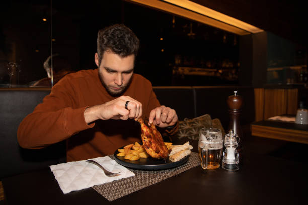 ein restaurantkunde isst sein essen, etwas hühnchen und pommes frites und ein bier. junger kaukasischer mann, der seine mahlzeit isst - catering, essen und trinken konzept - serving food restaurant chicken stock-fotos und bilder